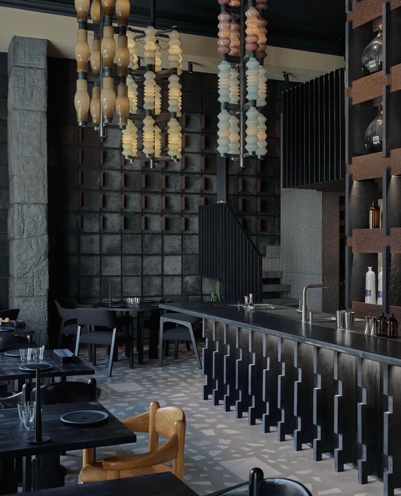 Dark stone-clad bar and dining counter in a restaurant, with pendant lighting and terrazzo flooring