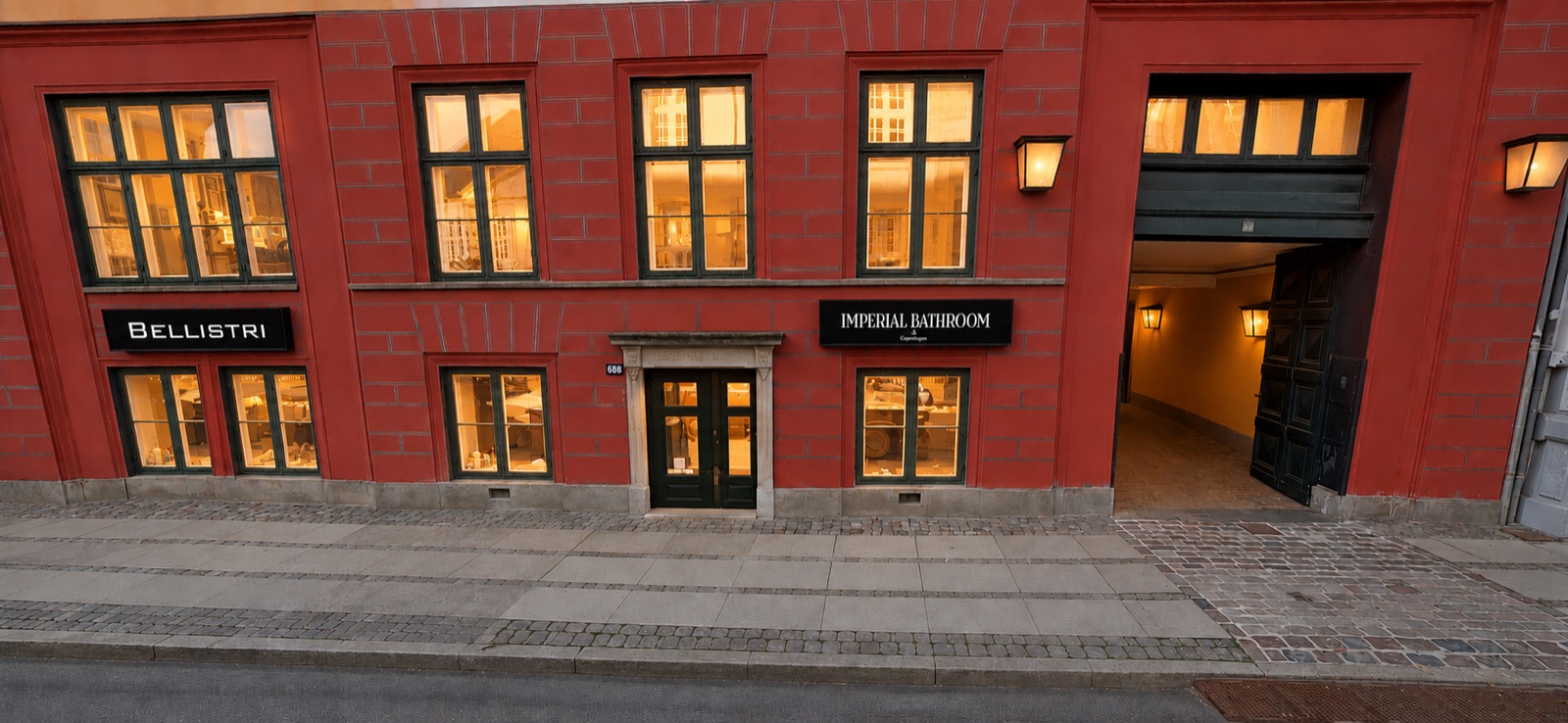 Bellistri showroom storefront on a red-brick Copenhagen street, illuminated at dusk
